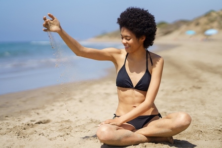 Content black woman pouring sand on shore in summer