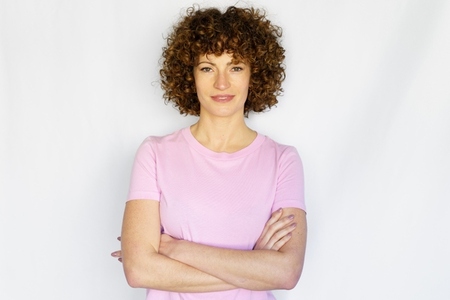 Adult woman with curly hair and crossed arms against white background