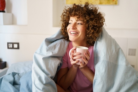 Happy woman enjoying coffee in bedroom