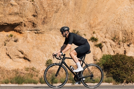 Side view of a cyclist in black sportswear riding his road bicycle