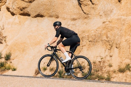 Male cyclist in black sportswear practicing on a countryside road