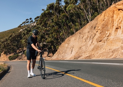 Male cyclist inspecting his bicycle while standing on a roadside on an empty road