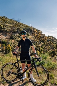 Male cyclist with bicycle in wild terrain looking at camera  Athlete in black sportswear with road bike relaxing