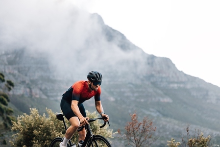 Professional male road bike rider exercising outdoors against the mountain with clouds
