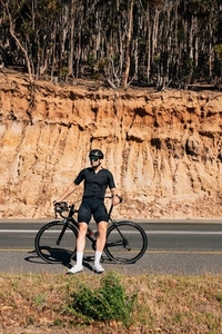 Male cyclist leaning his road bike while standing on a roadside