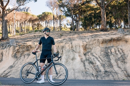 Athlete with road bicycle relaxing on a roadside looking away
