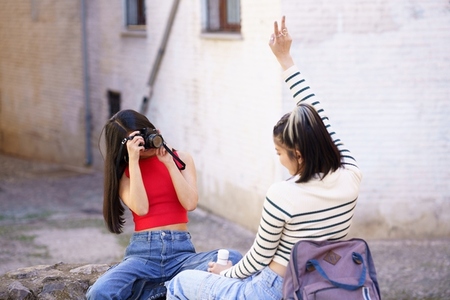 Woman taking photo of girlfriend on camera on street