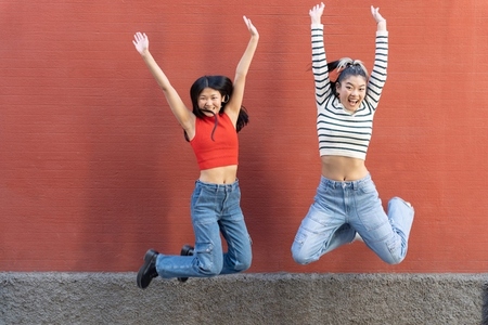 Excited Asian girlfriends jumping with arms up