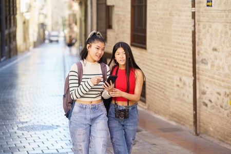 Asian female tourists walking on city street with smartphone