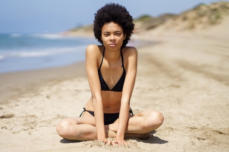 Serious black woman with Afro hair in bikini near sea