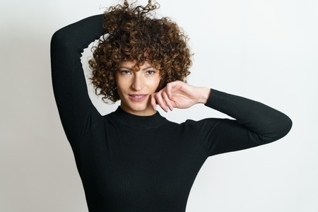 Happy female with curly hair smiling with hands near her head