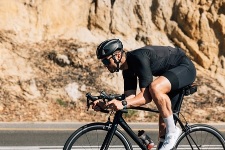 Professional road bike rider in black sportswear  Side view of a young male riding bicycle against a mountain