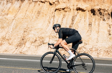 Professional triathlete in black sportswear riding road bike a hill on an empty road