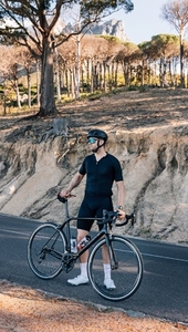 Full length of a triathlete with a bicycle standing on an empty road and looking away