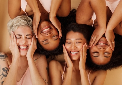 Happy girls touching their faces while lying together on a beige background  Smiling women with closed eyes massaging their cheeks with palms