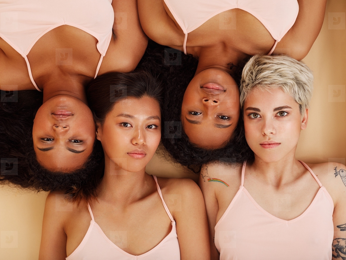 Group of four women lying together in a studio and looking at the camera  Diverse females lying head to head