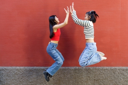 Joyful young Asian girlfriends giving high five while jumping