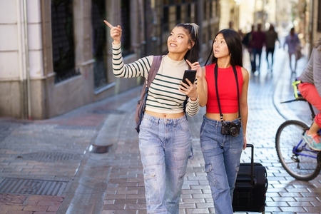 Asian female travelers pointing away while walking on street
