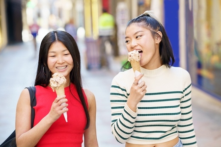 Smiling Asian girlfriends eating ice cream