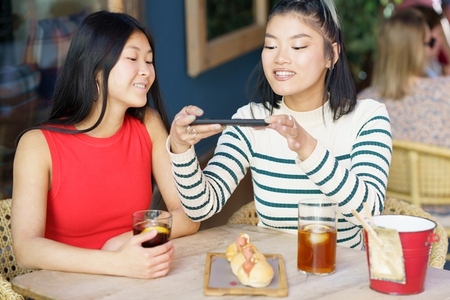 Delighted Asian women taking photo of food in cafe