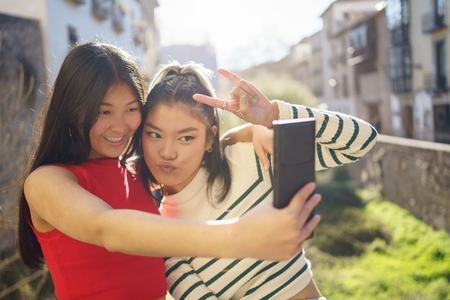 Smiling Asian girlfriends taking selfie on street