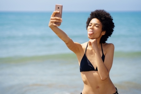 Happy black woman taking selfie on seashore in summer