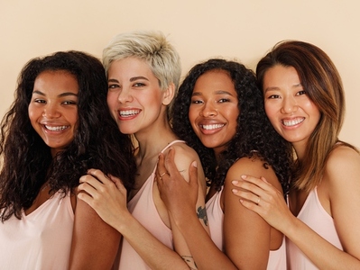 Group of smiling females standing together  Four women of different body types and skin tones looking at camera