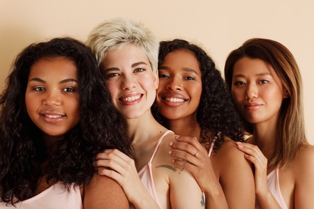 Four young females with different skin tones looking at the camera  Diverse women standing together