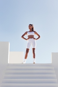 Full length of a slim confident woman looking away while standing on the top of stairs  Sportswoman in white fitness attire against skies