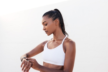 Fitness female in white sports attire adjusting smartwatch before a workout  Woman checking heart rate during training