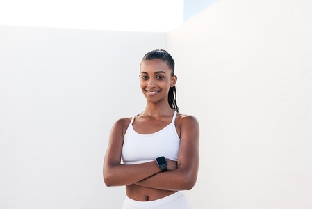 Portrait of a smiling woman in sportswear with crossed arms  Confident female athlete looking at camera outdoors