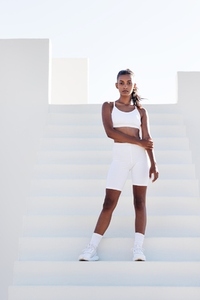 Full length slim fit female in white sports attire  Woman standing on white stairs relaxing during training