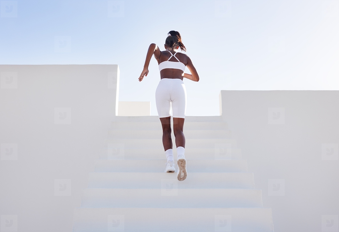 Back view of a woman in white sportswear running up on stairs. Rear view of a young female jogger exercising in a white outdoor studio