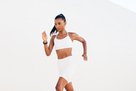 Slim female sprinter exercising outdoors at white wall  Young slim woman jogging at a day in white sportswear