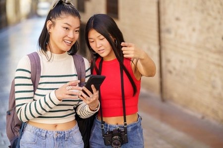 Asian girlfriends using map on smartphone while traveling together