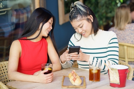 Positive Asian women taking picture of yummy food in cafe