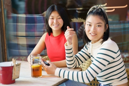 Joyful Asian women with beverages and smartphone in cafe