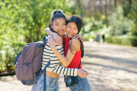 Happy Asian friends hugging in sunny forest during trip
