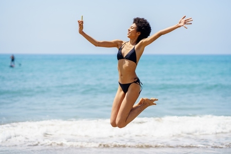 Black woman taking selfie while jumping near sea