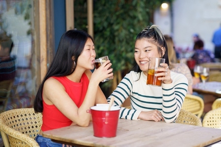 Smiling Asian friends drinking fresh beverages in cafe