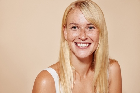 Cheerful blond female with perfect smooth skin looking at camera  Portrait of a happy freckled woman looking straight at a camera