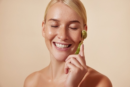 Happy woman with freckles and smooth skin using a jade stone roller