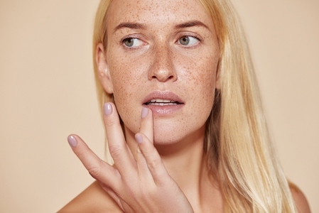 Woman with freckles touching her lip with a finger  Blond female with perfect skin applying balm on her lips