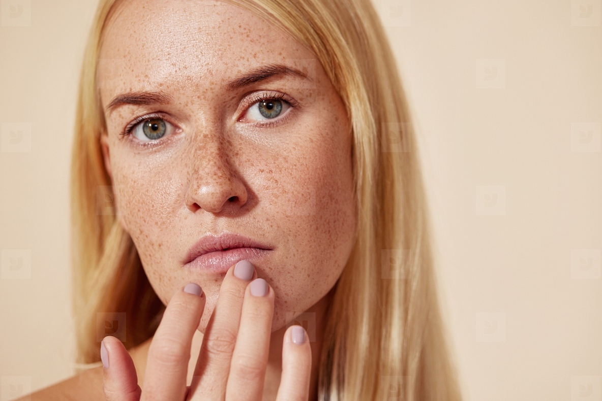 Close up of a woman with freckles touching her lip with a finger  Young blond female applying balm on her lips