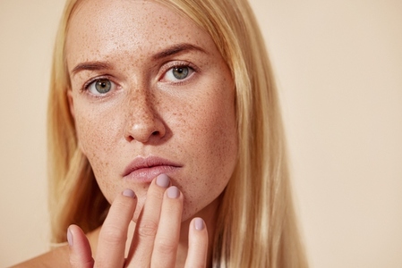 Close up of a woman with freckles touching her lip with a finger  Young blond female applying balm on her lips