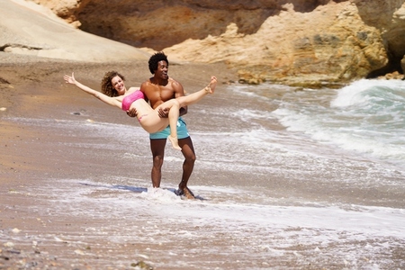 Young black man lifting up woman on beach