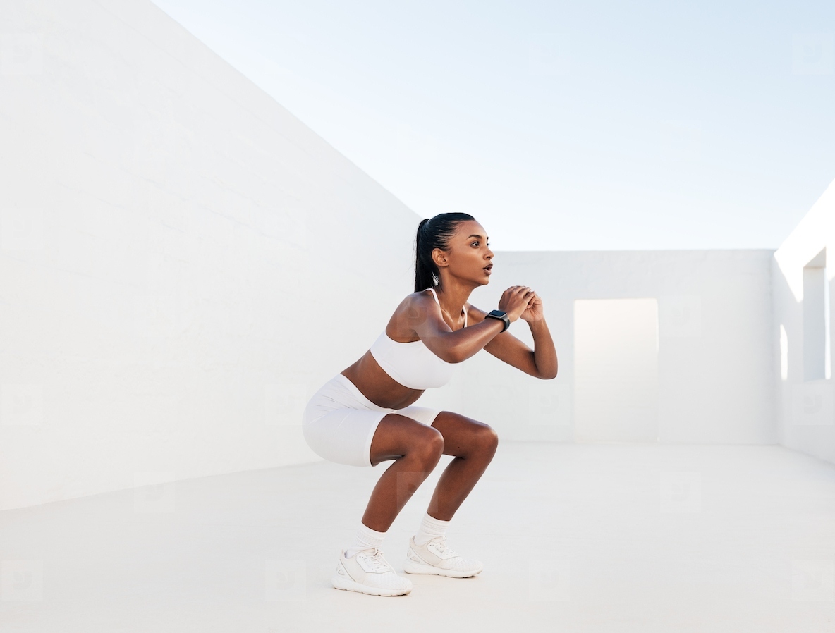 Female fitness influencer doing sit-ups in a white outdoor studio. Young woman doing workout outdoors. Female in white fitness attire is doing exercises for her glutes