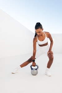 Young fit female doing a workout with a kettlebell  Woman exercising in a white outdoor studio with weights