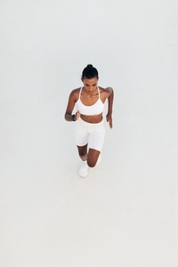 Shot from above of a young woman running in a white outdoor studio  High angle of a slim female sprinting