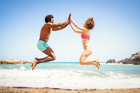 Happy multiethnic couple jumping near sea